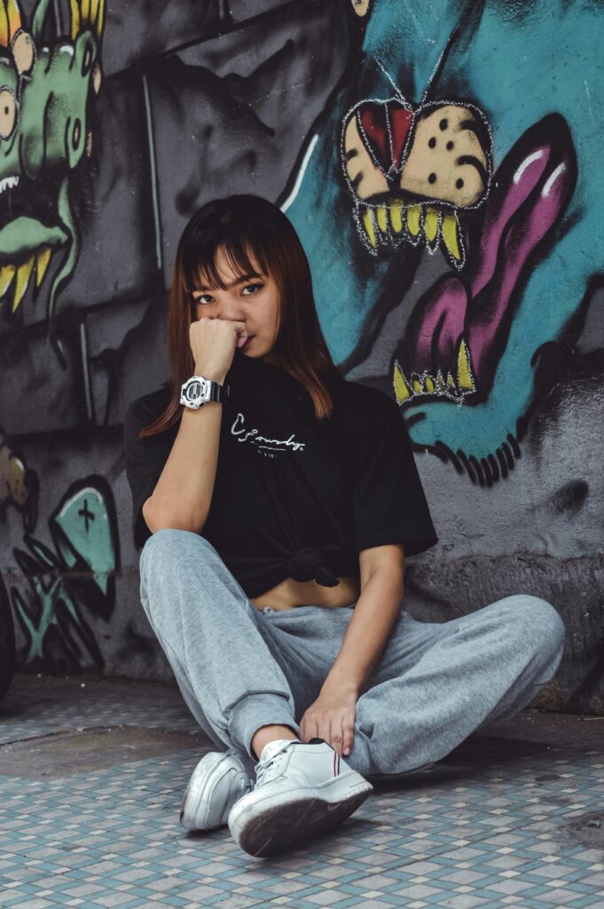 Young woman in casual streetwear sitting thoughtfully against a vibrant graffiti wall.